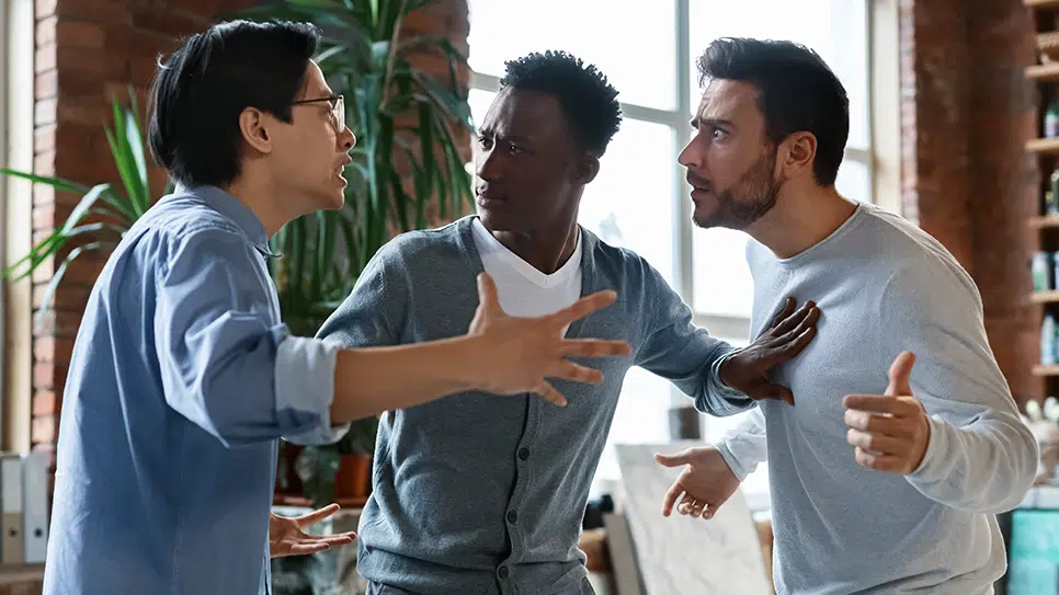 one man breaking up an argument between two other men in an office setting