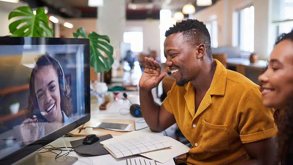 A Black man waves to his colleague on a video call from his office