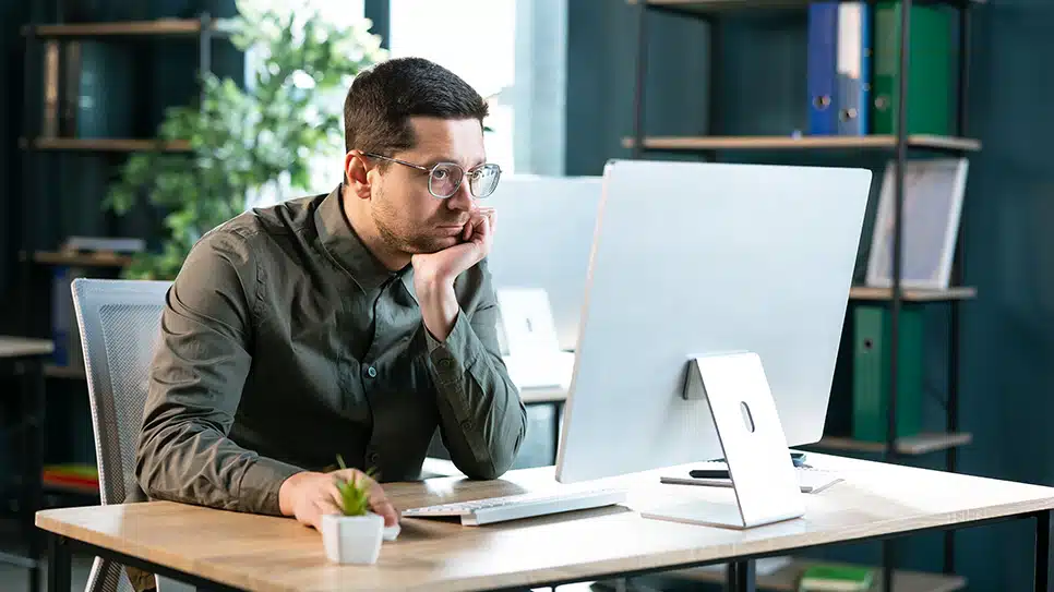Portrait of sad bored business man sitting at desk using pc, lea